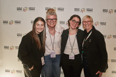 Carolyne De Bellefeuille, Katia Aubin, Marika Roberts, and Martine Roy in front of a Pride at Work Canada's backdrop.
